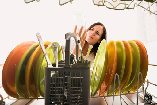 A woman closely inspecting a glass that she put in the dishwasher.